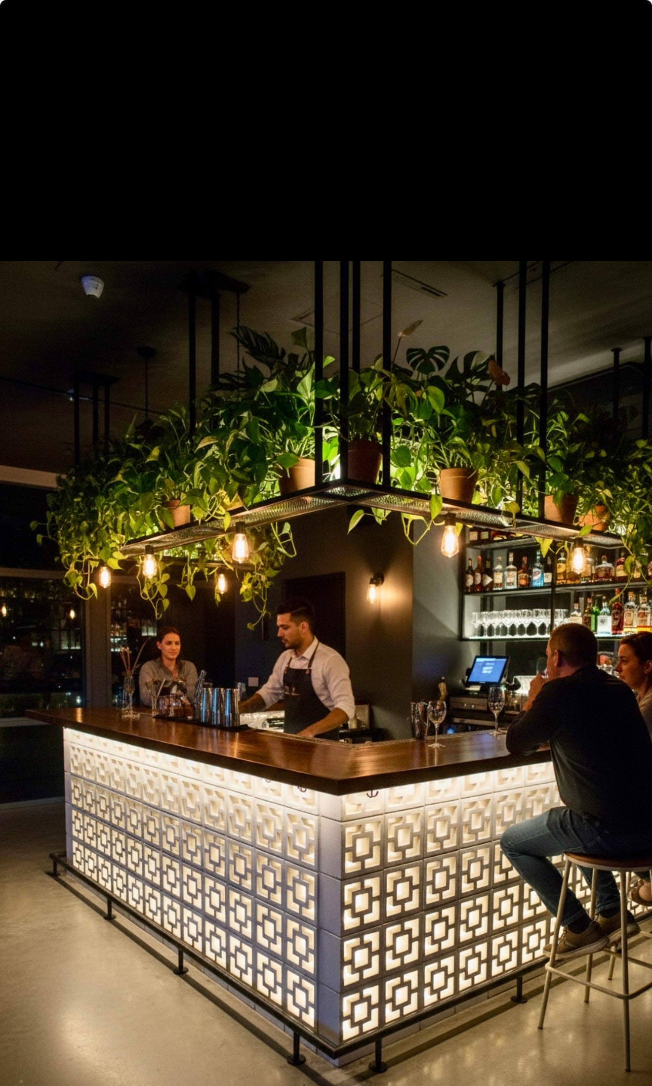 Tong bar features a glowing geometric counter by New York Cement Tile, breeze block partitions, hanging plants, and warm lights.