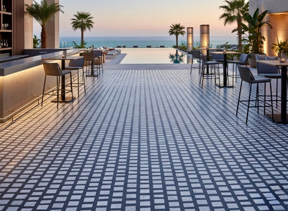Outdoor poolside lounge with palm trees and tables, featuring Carlo Scarpa- Dark Gray tiles by New York Cement Tile.