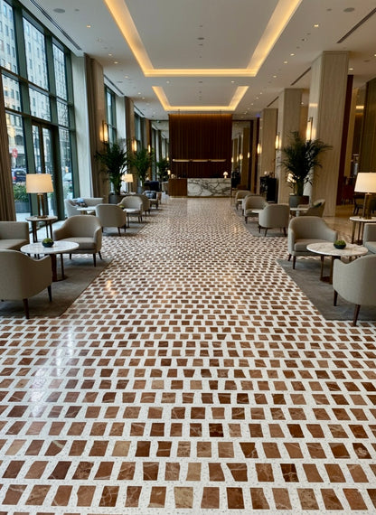 Modern hotel lobby featuring Carlo Scarpa- Earth tiles by New York Cement Tile, armchairs, tables, tall windows, and plants.