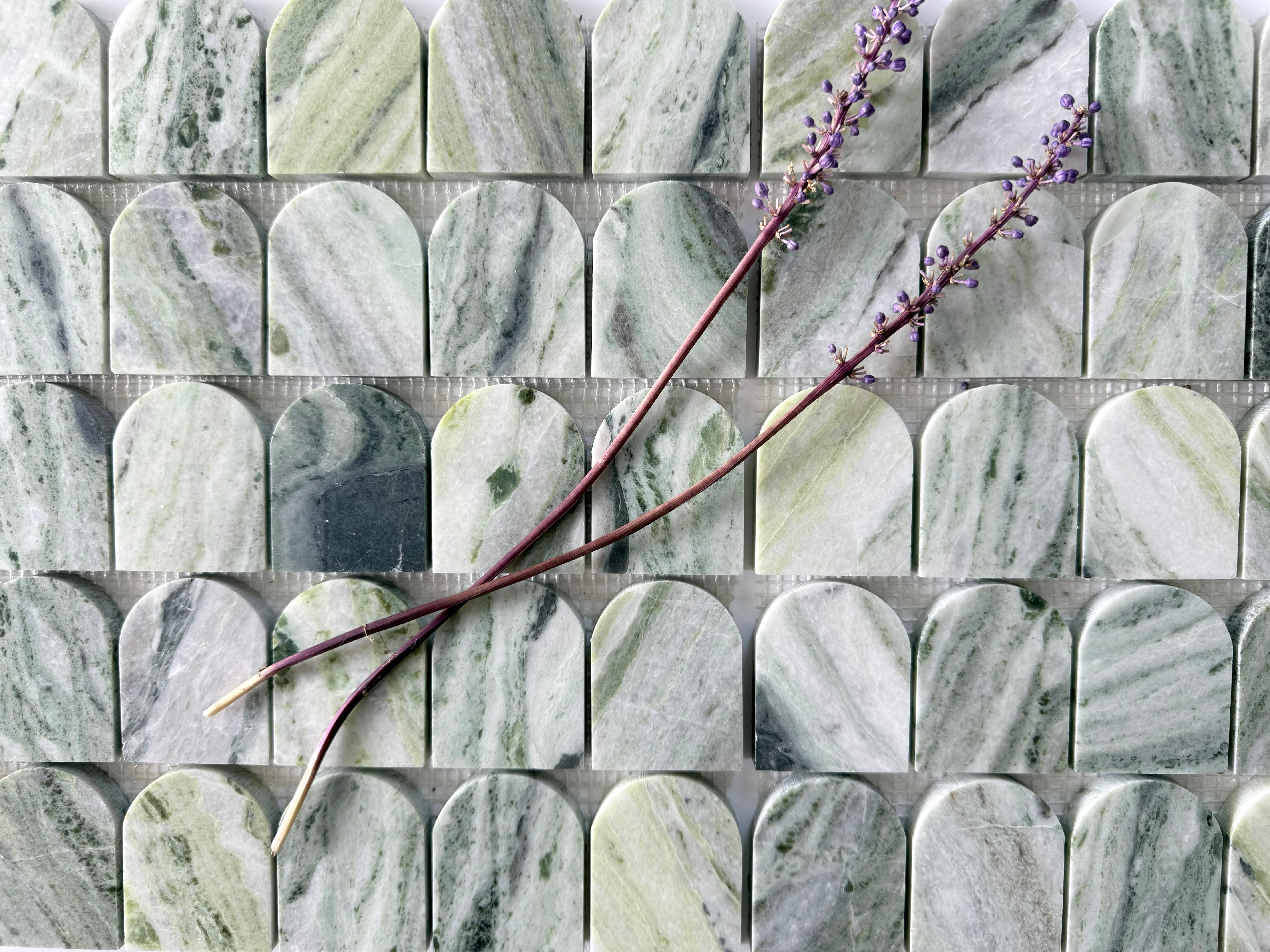 Two sprigs of lavender rest on Scarpa I Green Vibes Arch Mosaic Marble Mesh by New York Cement Tile, inspired by Italian design.