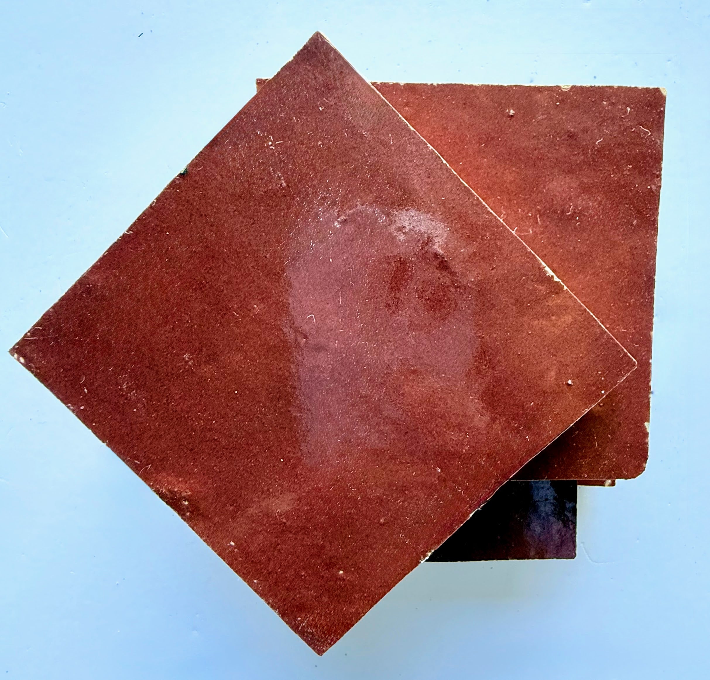 Two Chocolate Cherry tiles by New York Cement Tile on blue, reflecting the textured charm of handcrafted surfaces.
