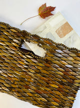 A Carlo Scarpa - Mountain High tile by New York Cement Tile, a beaded brown clutch, and a red maple leaf on white.