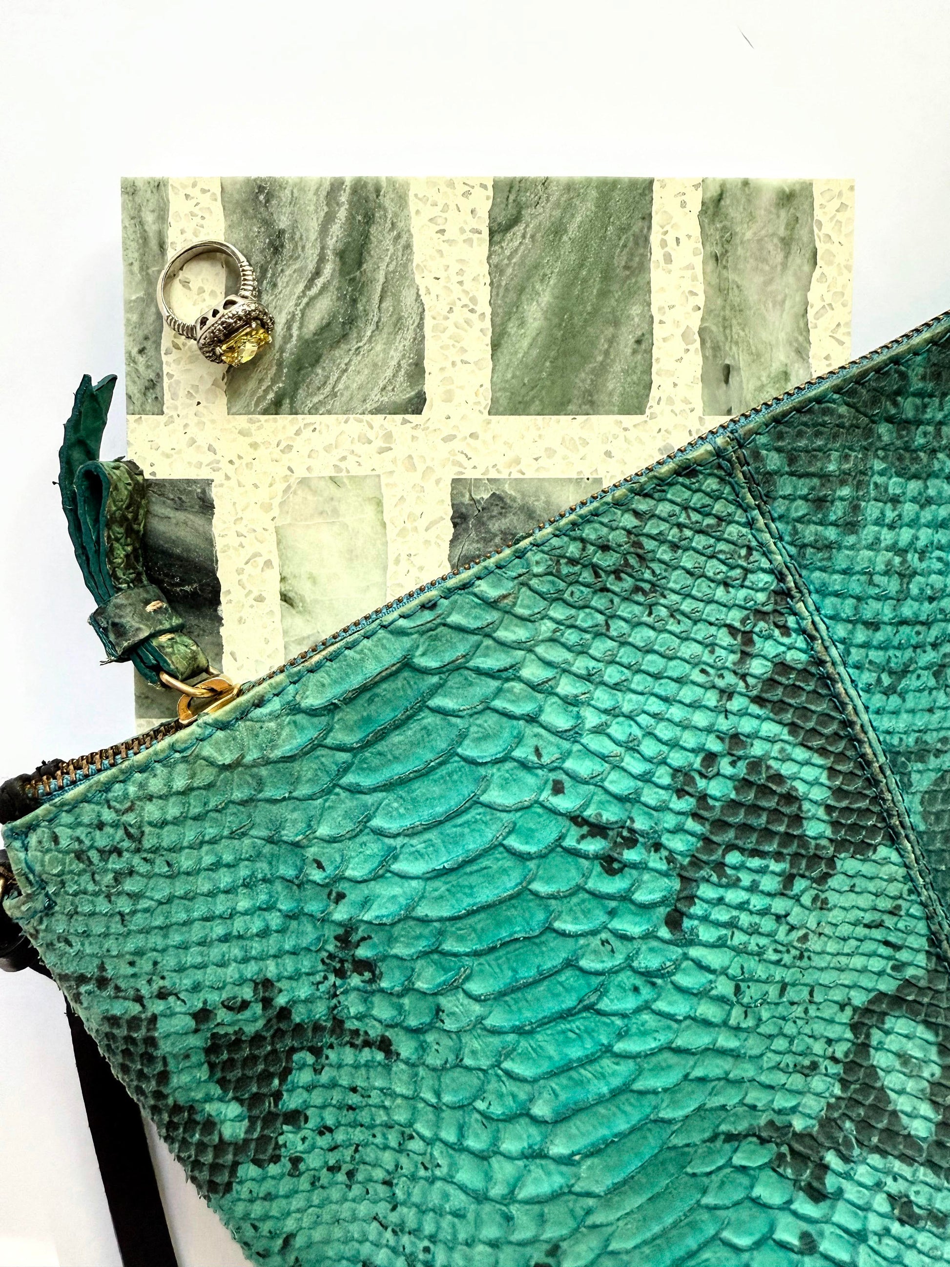 A teal snakeskin clutch, a yellow stone ring, and New York Cement Tile’s Carlo Scarpa - Green Vibes tile on white.