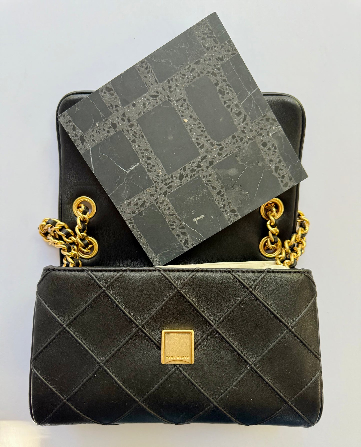 A Carlo Scarpa- Black purse by New York Cement Tile opens to reveal a black patterned notebook inside.