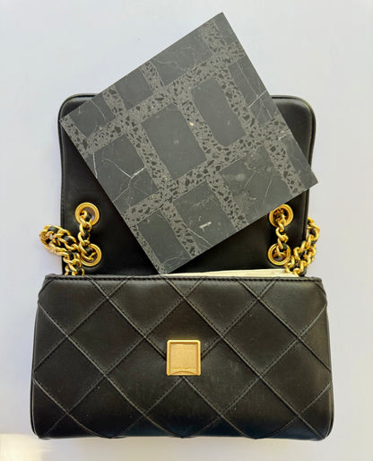 A Carlo Scarpa- Black purse by New York Cement Tile opens to reveal a black patterned notebook inside.