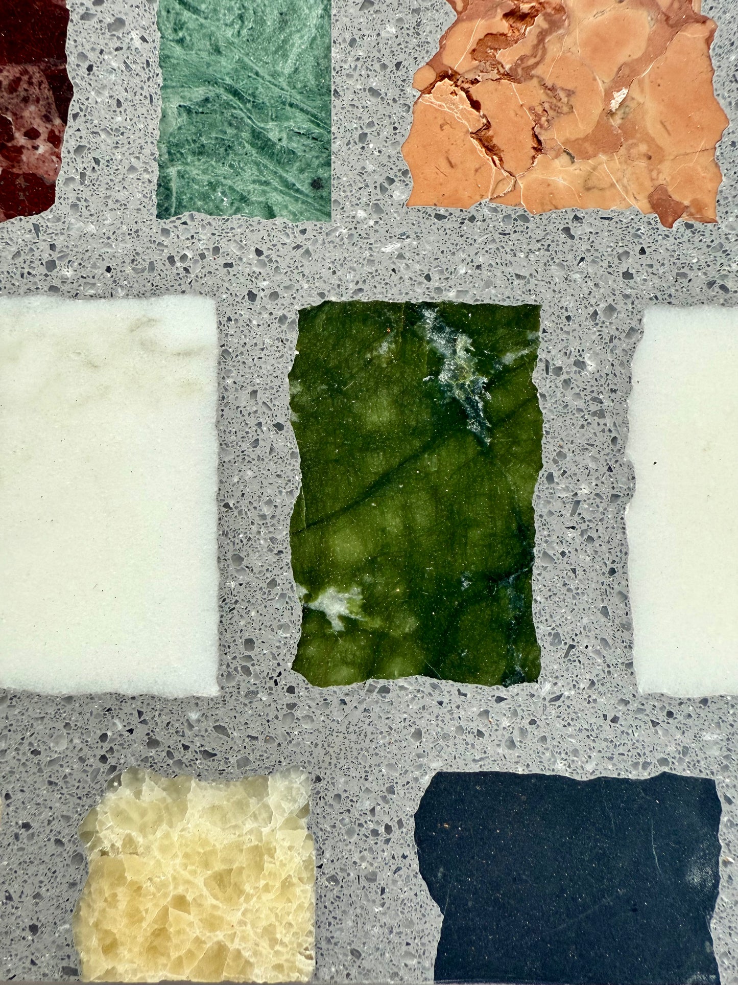 Carlo Scarpa- Multicolor Dark tiles by New York Cement Tile are arranged in a grid on a speckled gray background.