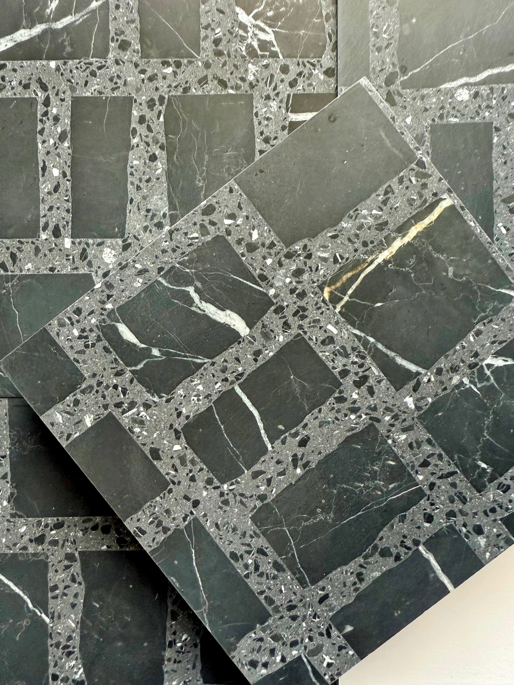 Carlo Scarpa- Black by New York Cement Tile: black and gray grid-patterned tile with white veining, one stacked diagonally.