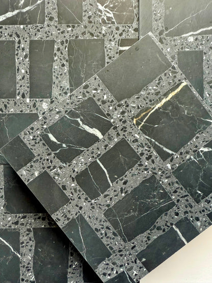 Carlo Scarpa- Black by New York Cement Tile: black and gray grid-patterned tile with white veining, one stacked diagonally.