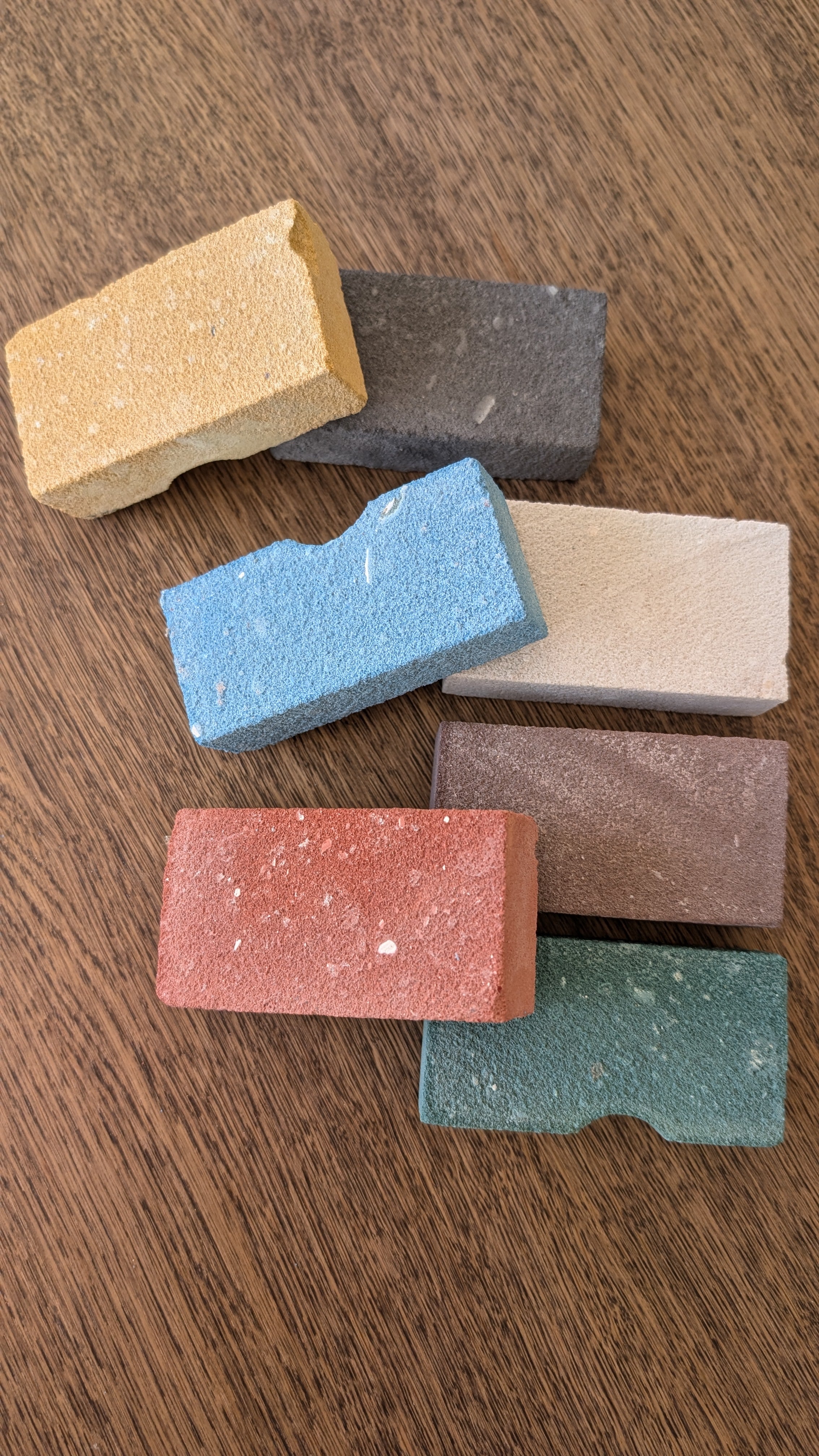 Seven colorful rectangular blocks arranged on a wooden surface; each block is a different color and texture.
