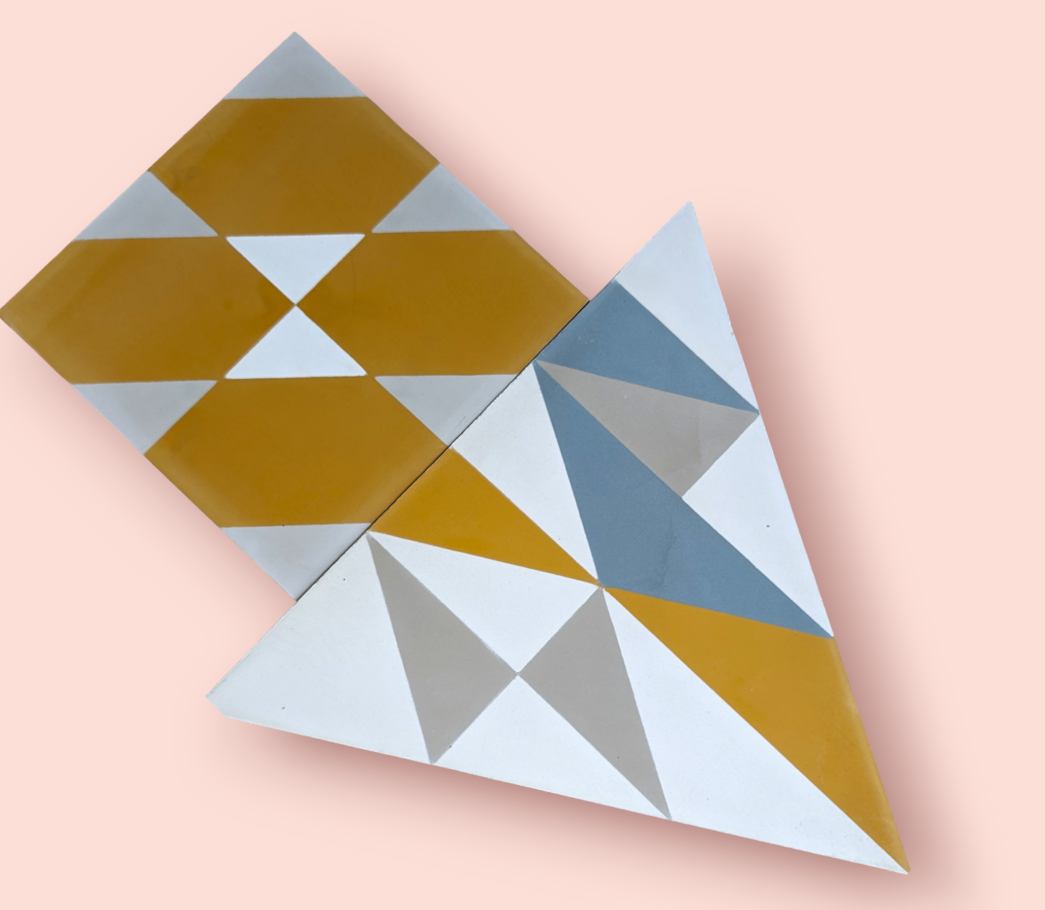 Two geometric tiles with yellow, gray, and white triangles, arranged on a light pink background.