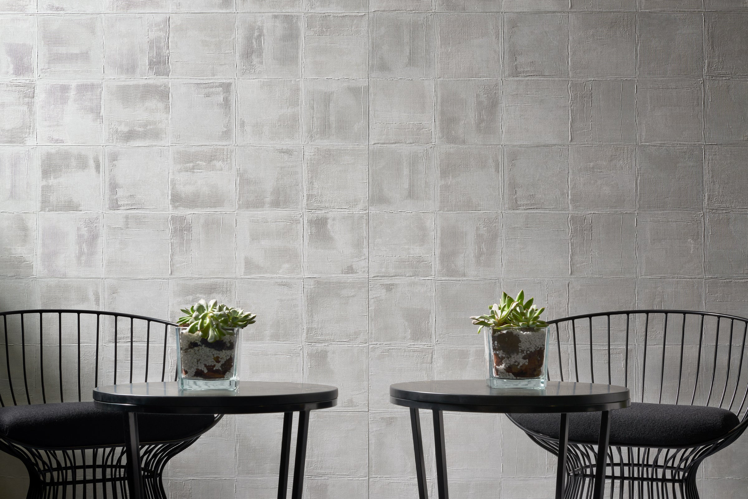Two black wire chairs and tables with succulents sit by a Gray Plaster wall from New York Cement Tile.