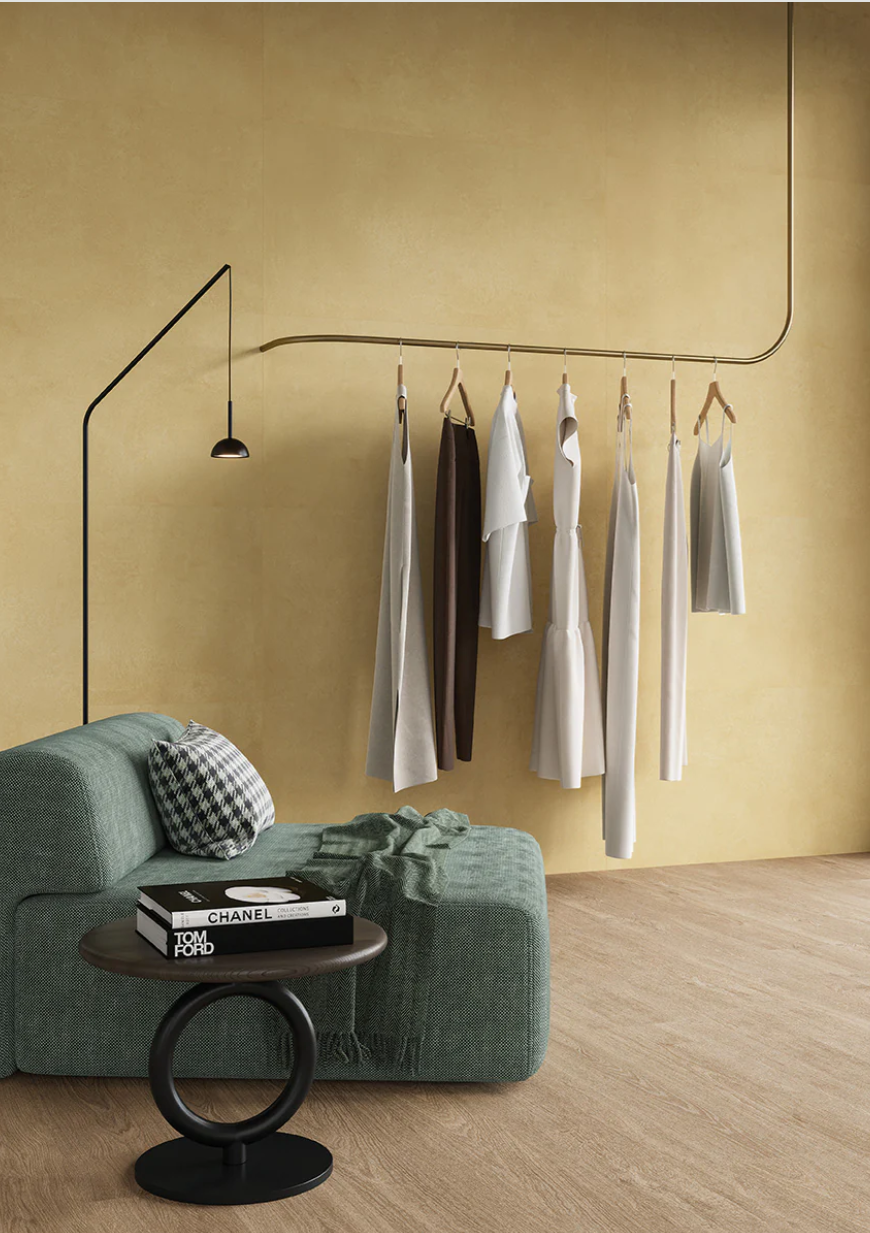 Minimalist room featuring clothes, books, a green sofa, and New York Cement Tile’s AGIO 24" x 47" SLIM- Senape tiles.