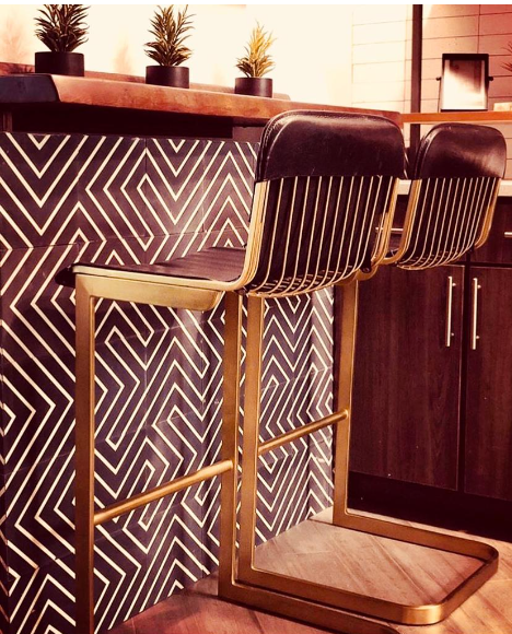 Two modern bar stools with gold frames at a counter with geometric tile and small potted plants.