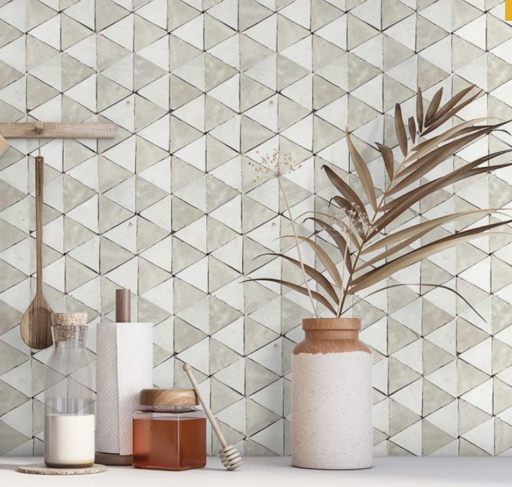 Kitchen counter with honey jar, spices, paper towel, utensils, and a vase with dried leaves against a geometric tiled wall.