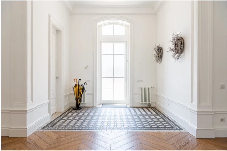 Bright entryway with a large windowed door, tiled floor, umbrella stand, and decorative wall wreaths.