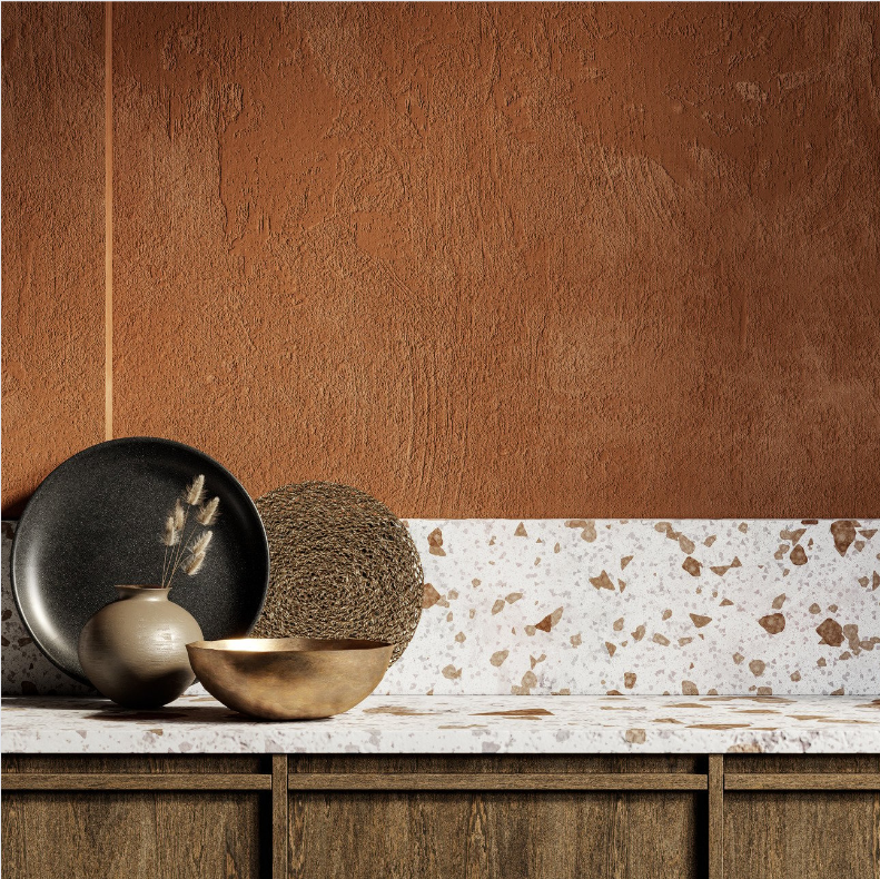 Rust-colored textured wall with a terrazzo countertop and decorative bowls and vases arranged on a wooden cabinet.