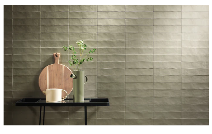 A small table with a cutting board, a vase with green foliage, and a teapot against a tiled wall.