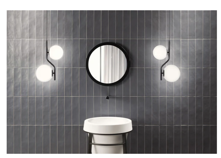 Modern bathroom with a round mirror, white sink, and two globe pendant lights on a dark tiled wall.