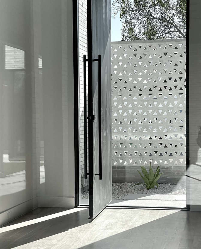 Modern glass door open to a small patio with a geometric white privacy wall and a single agave plant. Sunlight casts shadows.