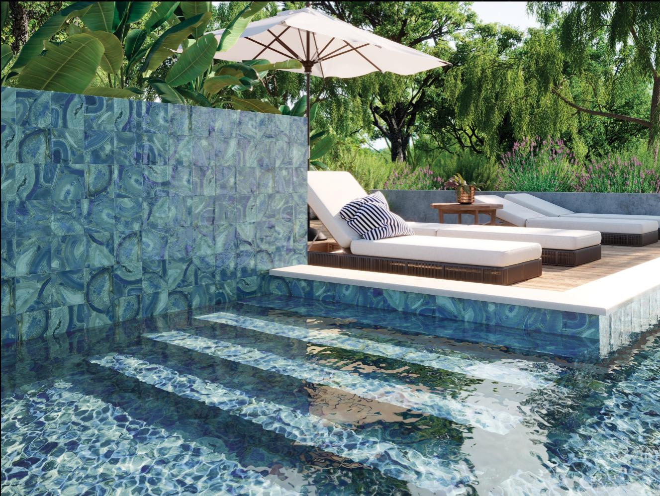 A pool with blue mosaic tiles, lounge chairs, and an umbrella surrounded by greenery on a sunny day.