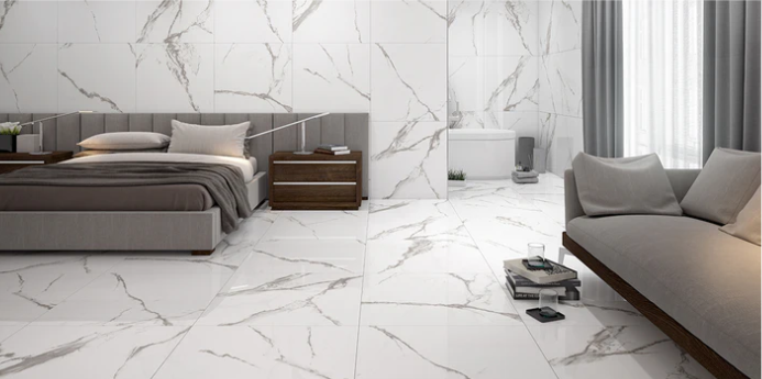 Modern bedroom and bathroom with large white marble tiles, grey bed and sofa, wooden furniture, and floor-to-ceiling curtains.