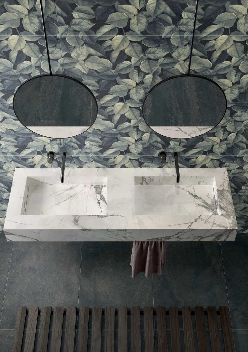 Marble double sink with black faucets, two round mirrors, leafy wallpaper, and a towel hanging between the sinks.