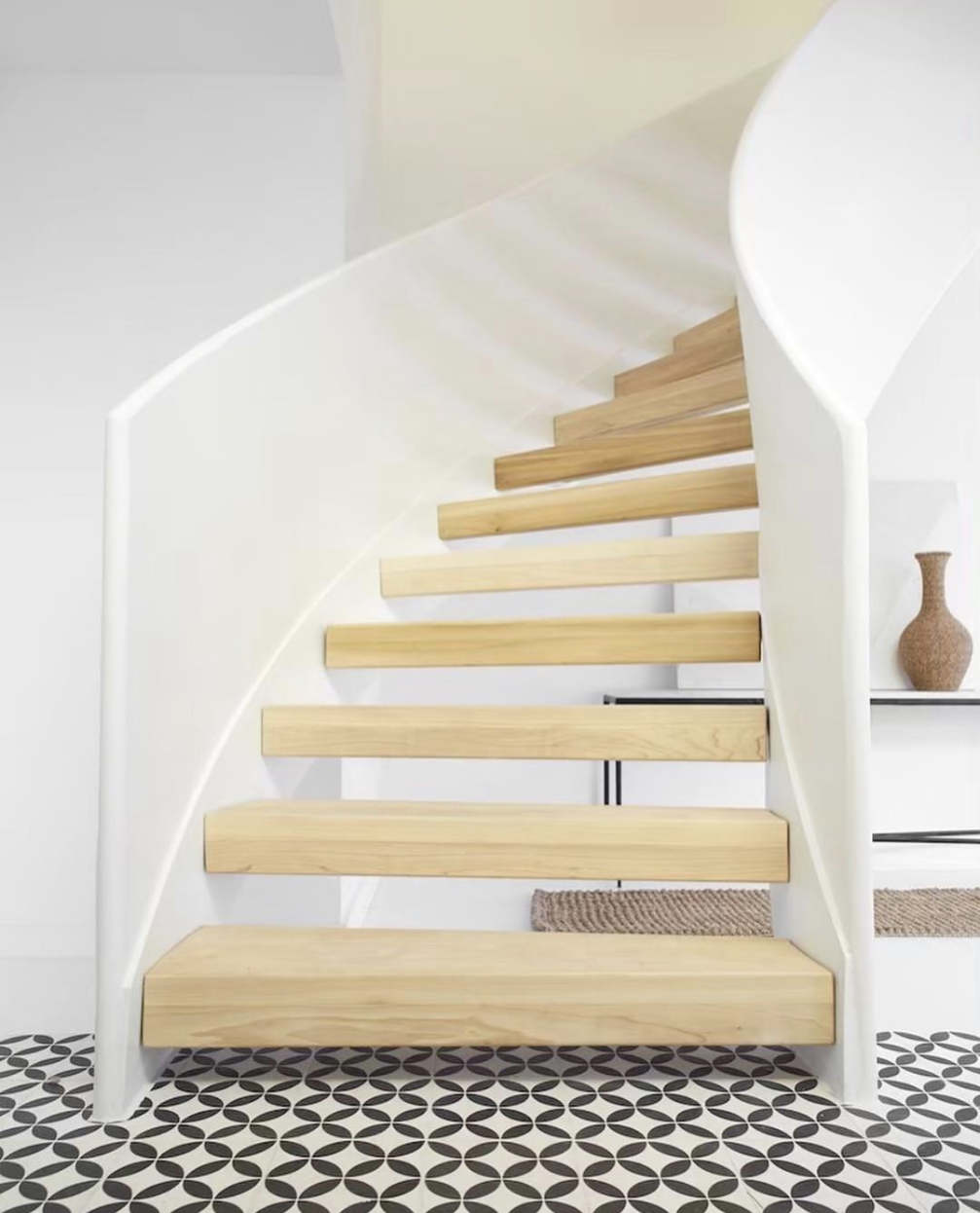 A modern spiral staircase with light wood steps and white railings, set on black and white patterned floor tiles.