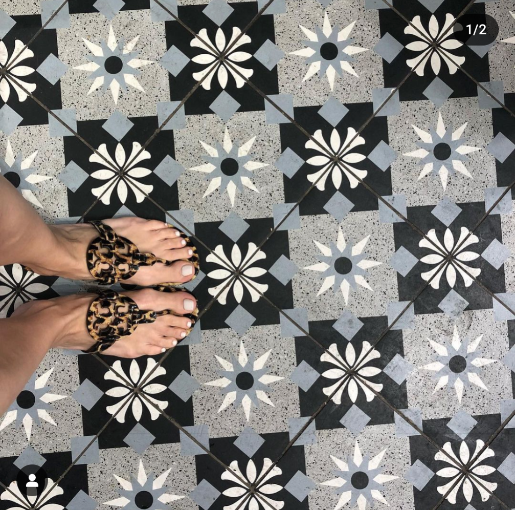 Feet in leopard print sandals standing on black, white, and gray geometric patterned floor tiles with floral designs.