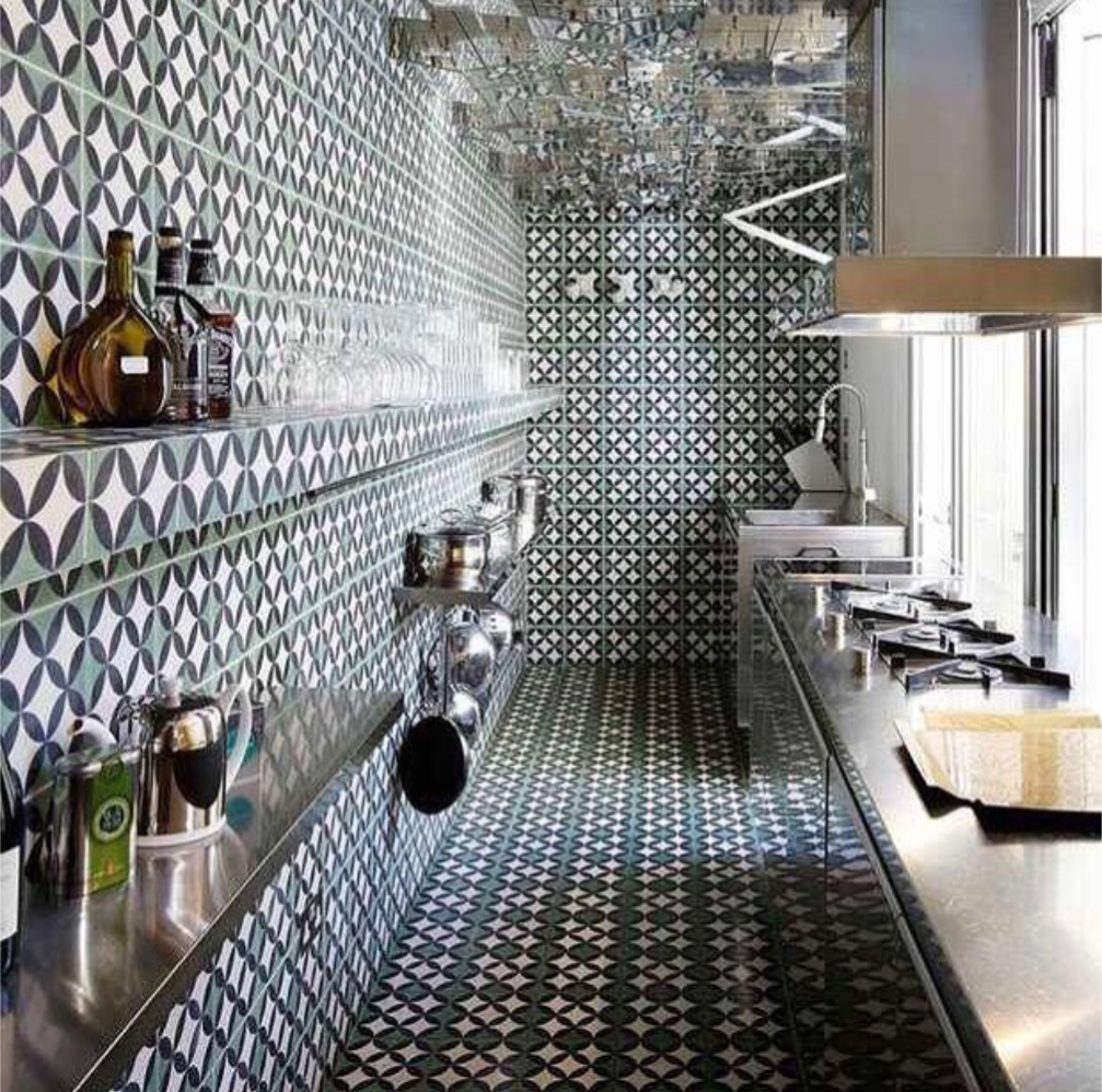 Modern galley kitchen with geometric patterned tiles on floor, walls, and ceiling, and stainless steel counters and shelves.