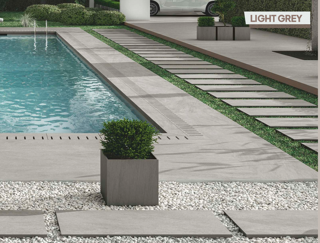 Modern poolside with light grey stone tiles, stepping stones, green lawn, potted plant, and a white car in the background.
