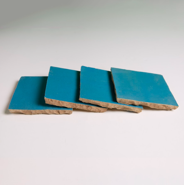 Four Azure tiles by New York Cement Tile in blue with rough beige edges are unevenly stacked on a white surface.