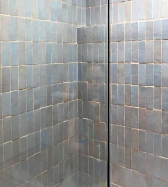 A shower corner with Arctic Blue (2X6) tile by New York Cement Tile, divided by a vertical glass panel.