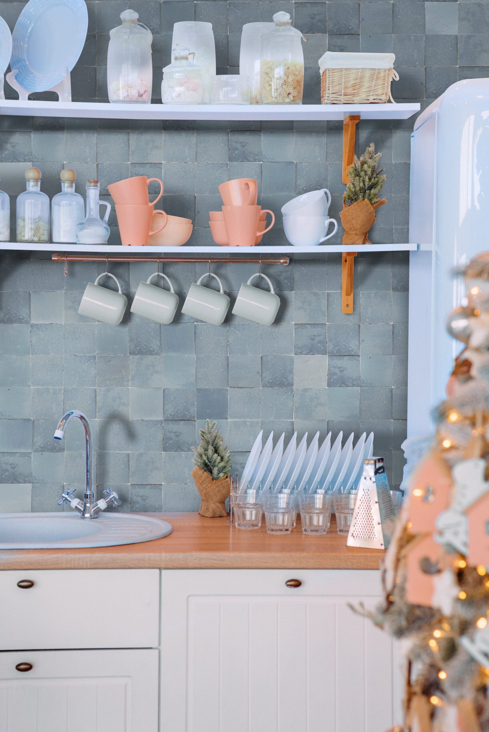 Ash Grey tiles by New York Cement Tile and pastel kitchenware on shelves above the sink add charm to the space.