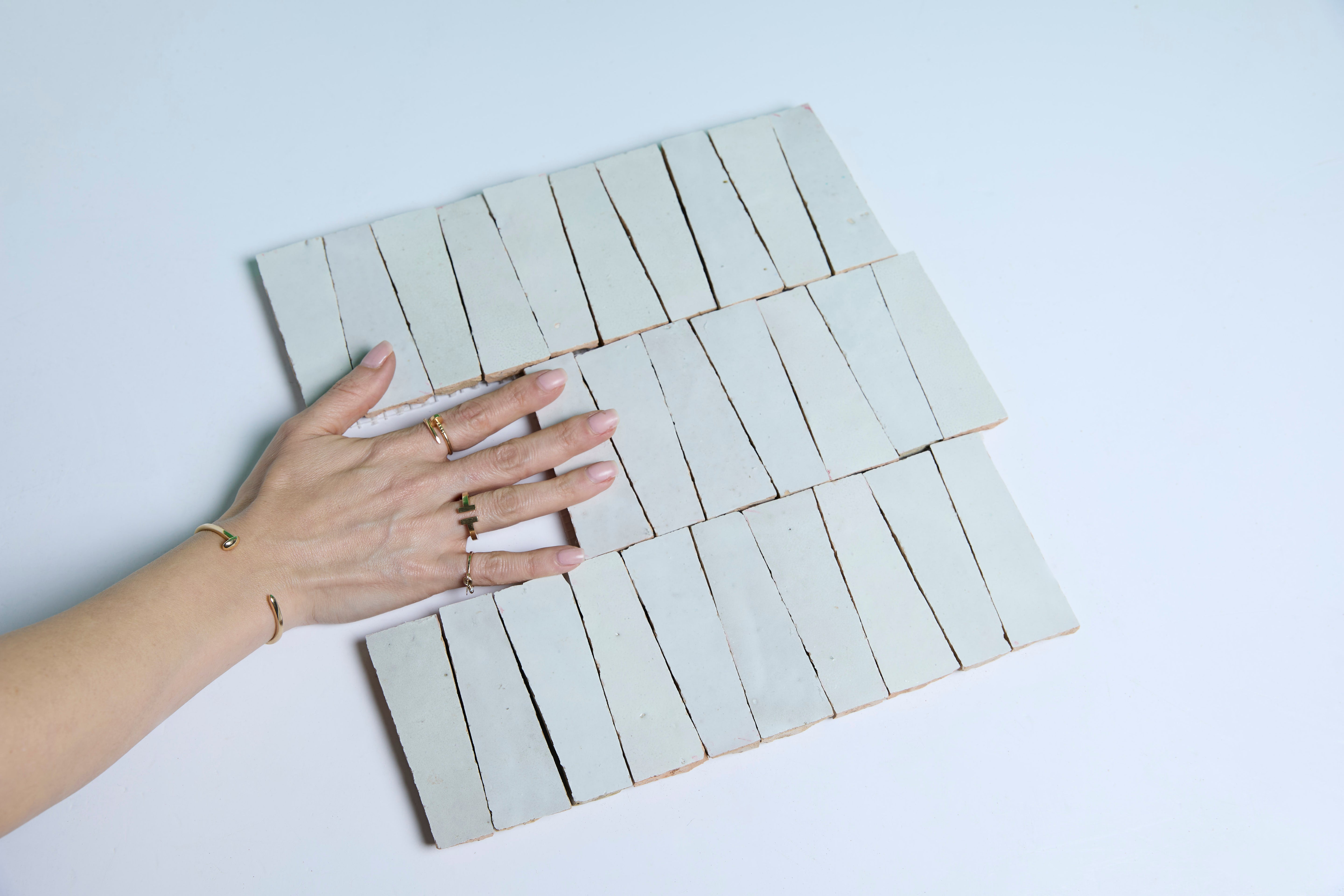 A hand with rings touches white rectangular tiles arranged in rows on a light surface.