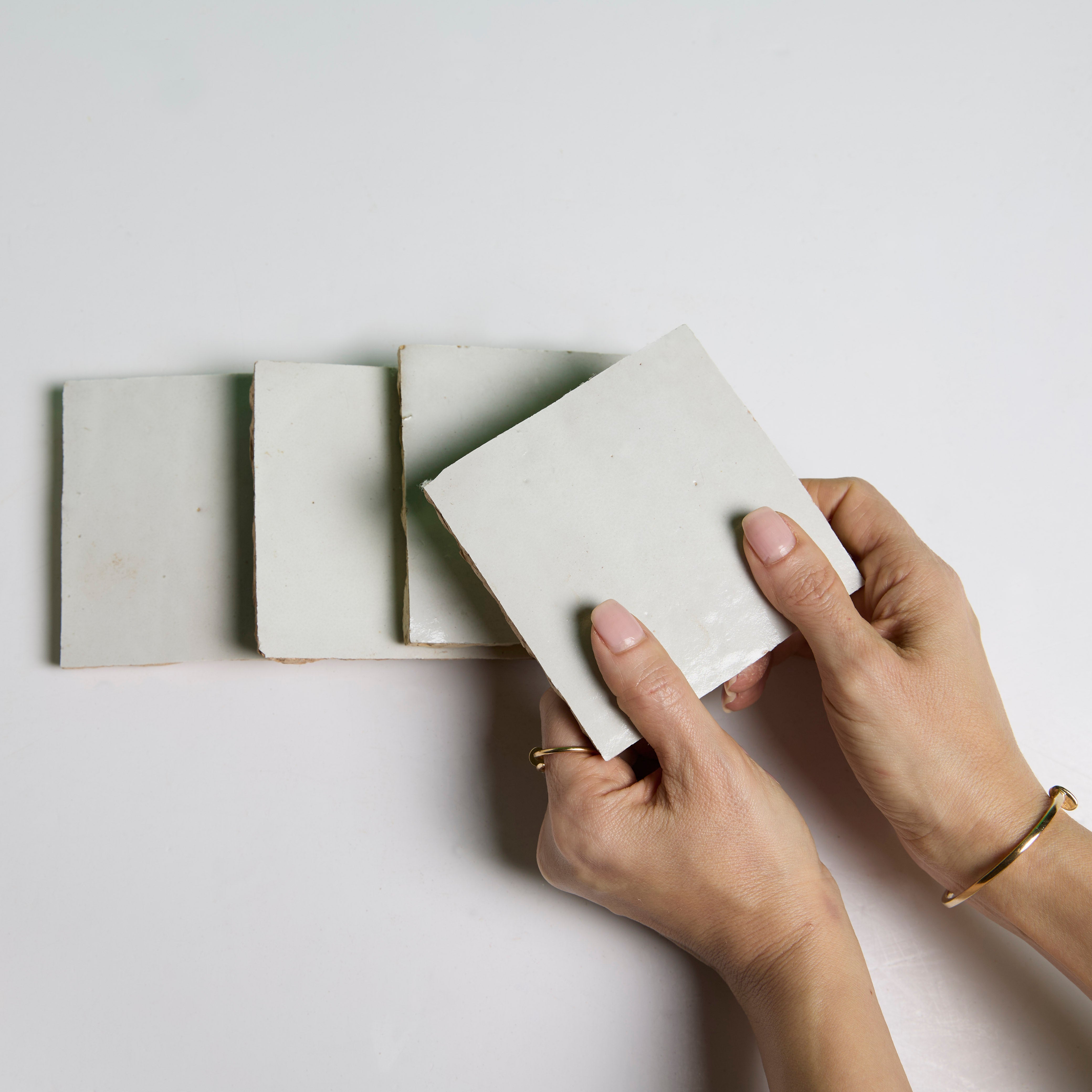 A person holds a New York Cement Tile "Ivory Cloud" tile above three similar tiles on a white surface.