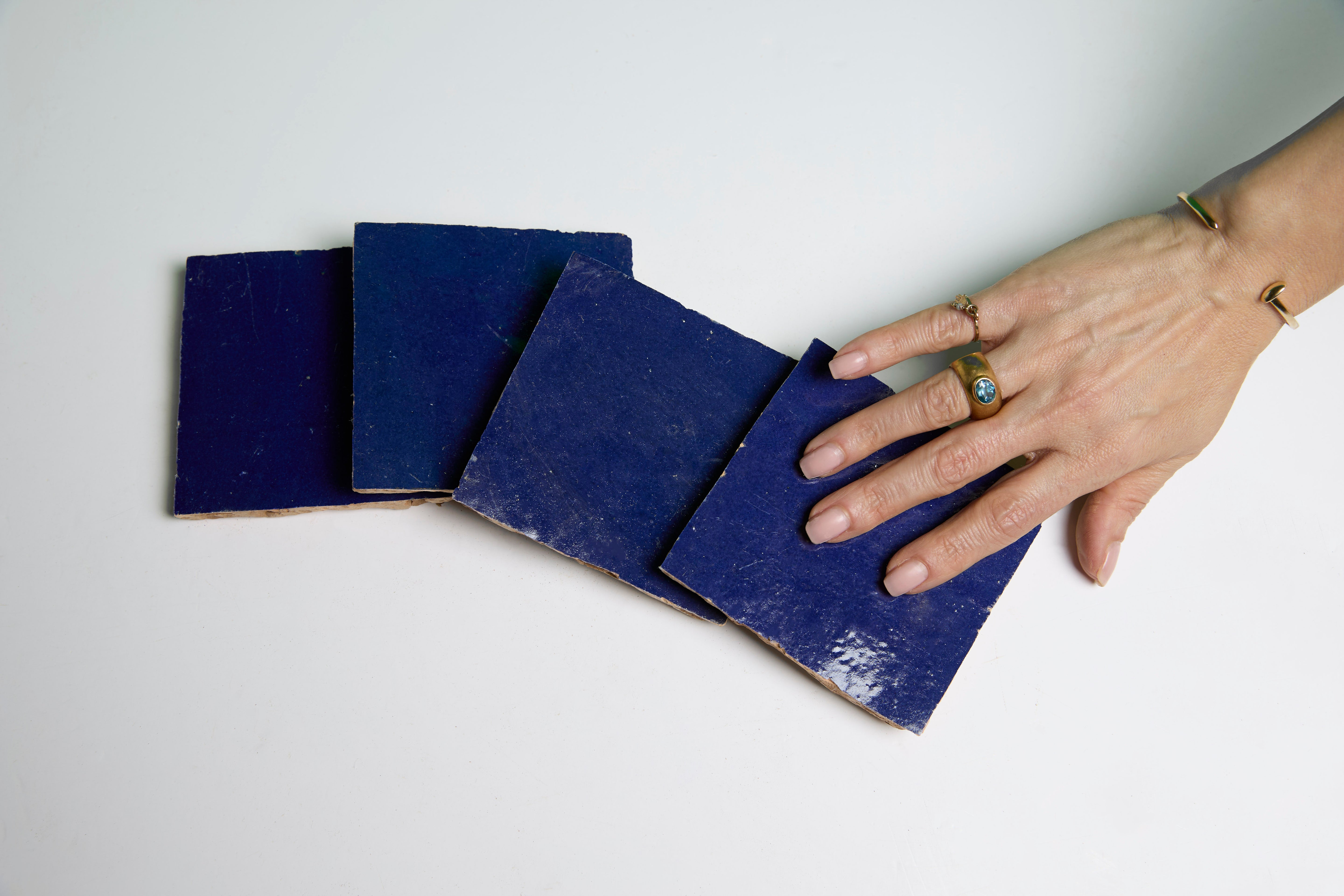 A hand with rings touches four Navy Depths tiles by New York Cement Tile, arranged on a white surface.