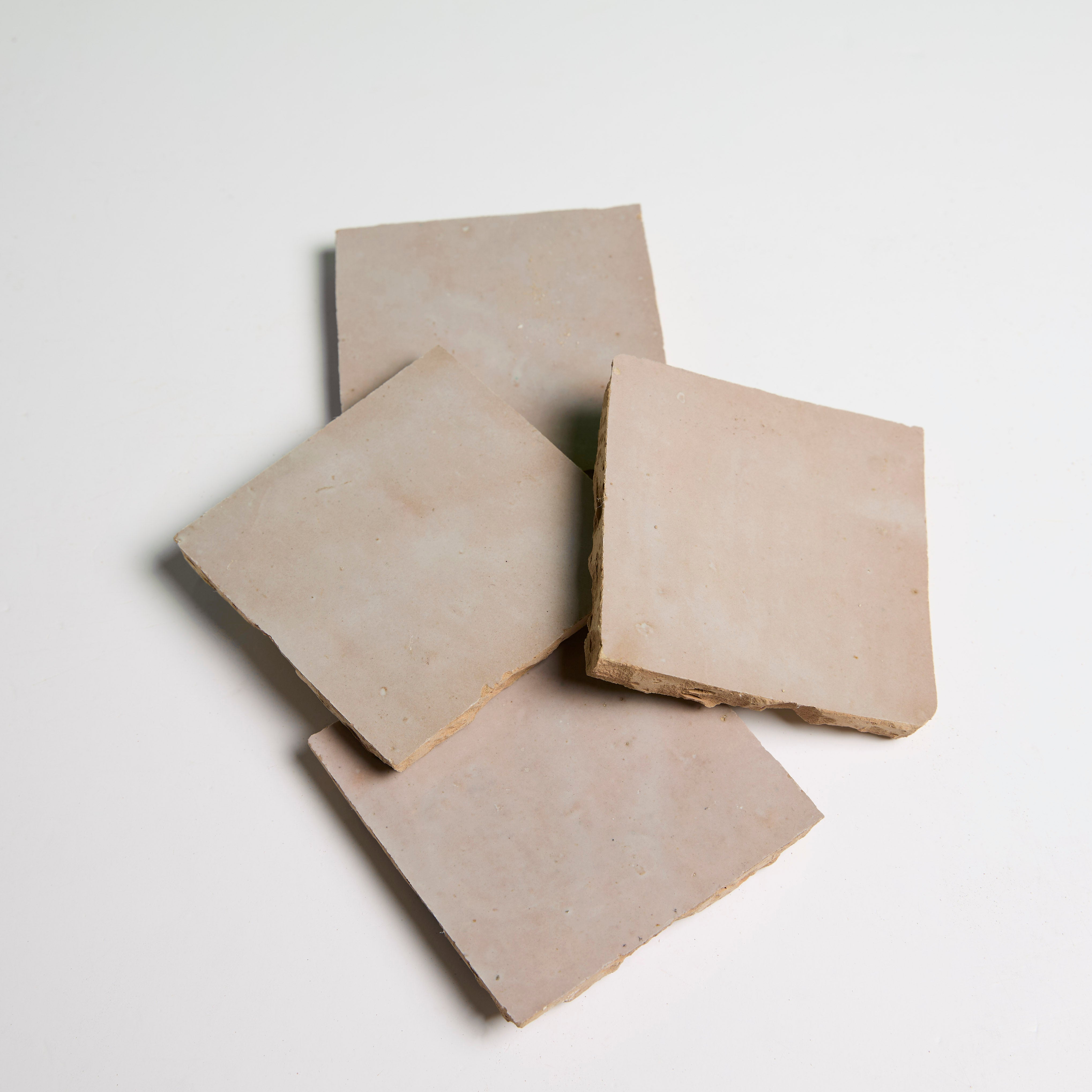Four Blushed Glazed tiles by New York Cement Tile overlap in a scattered arrangement on a white background.