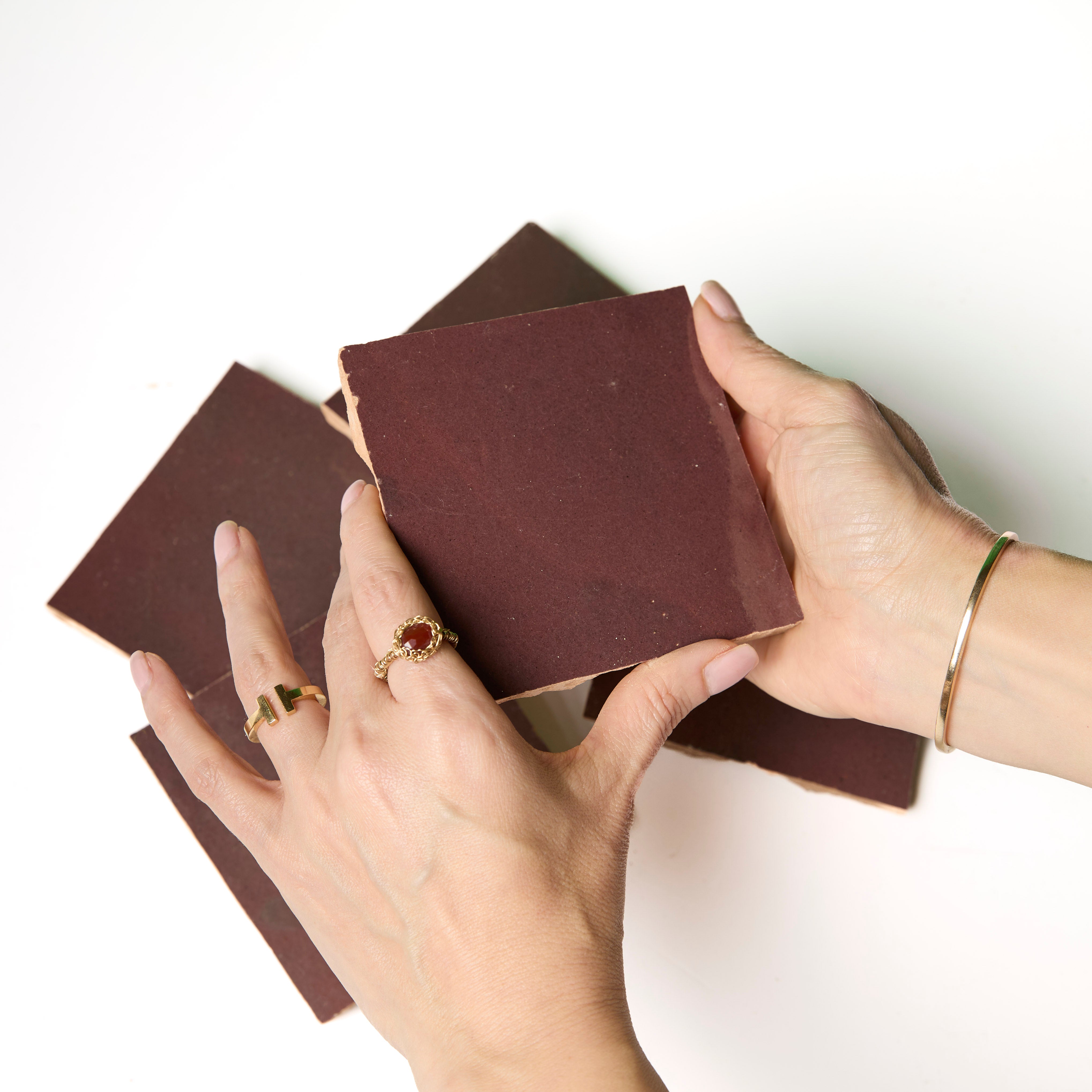 A person with rings and a bracelet preps New York Cement Tile's Thistle tile on a clean white surface.