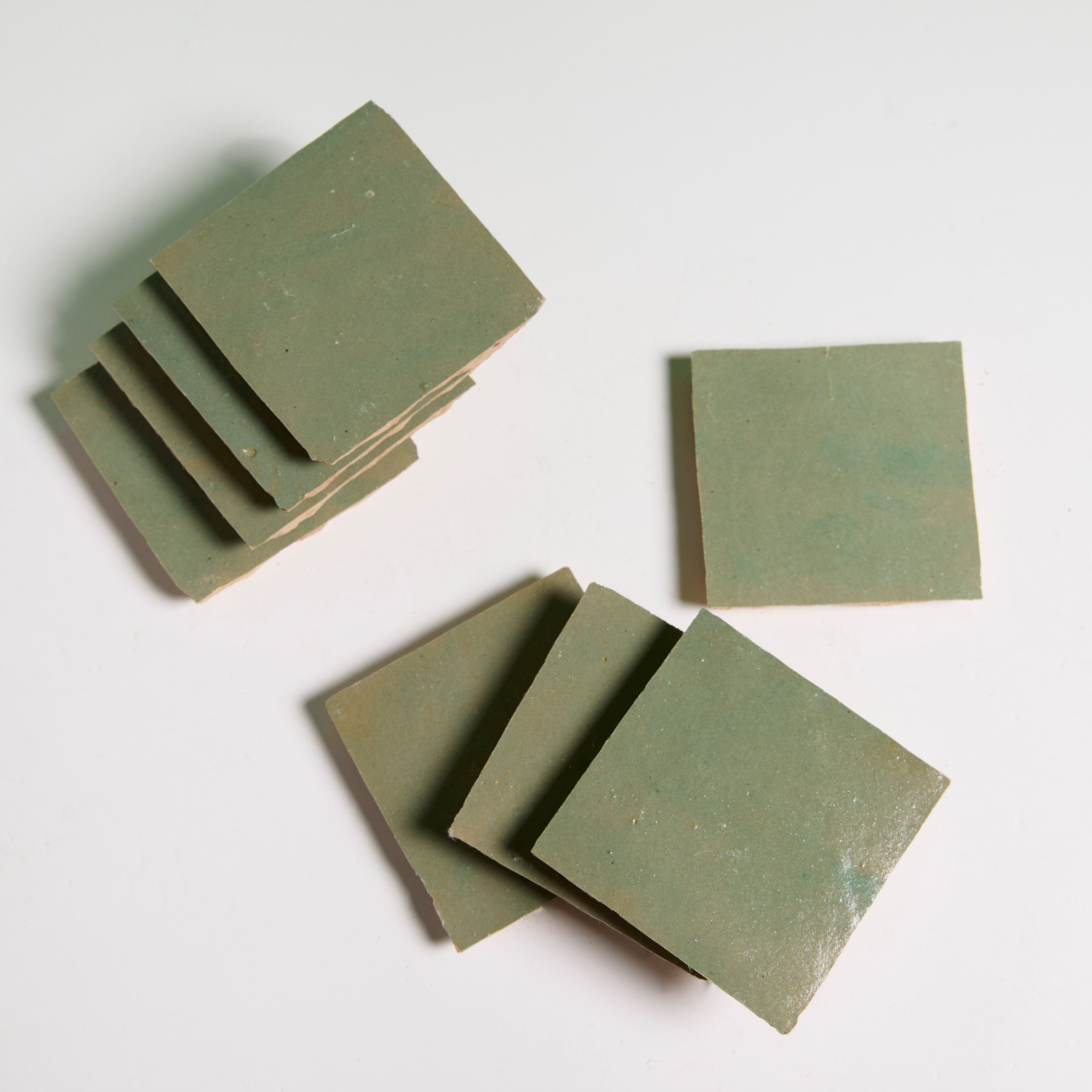 Leafy Green square Zellige tiles by New York Cement Tile are stacked and spread out on a white surface.
