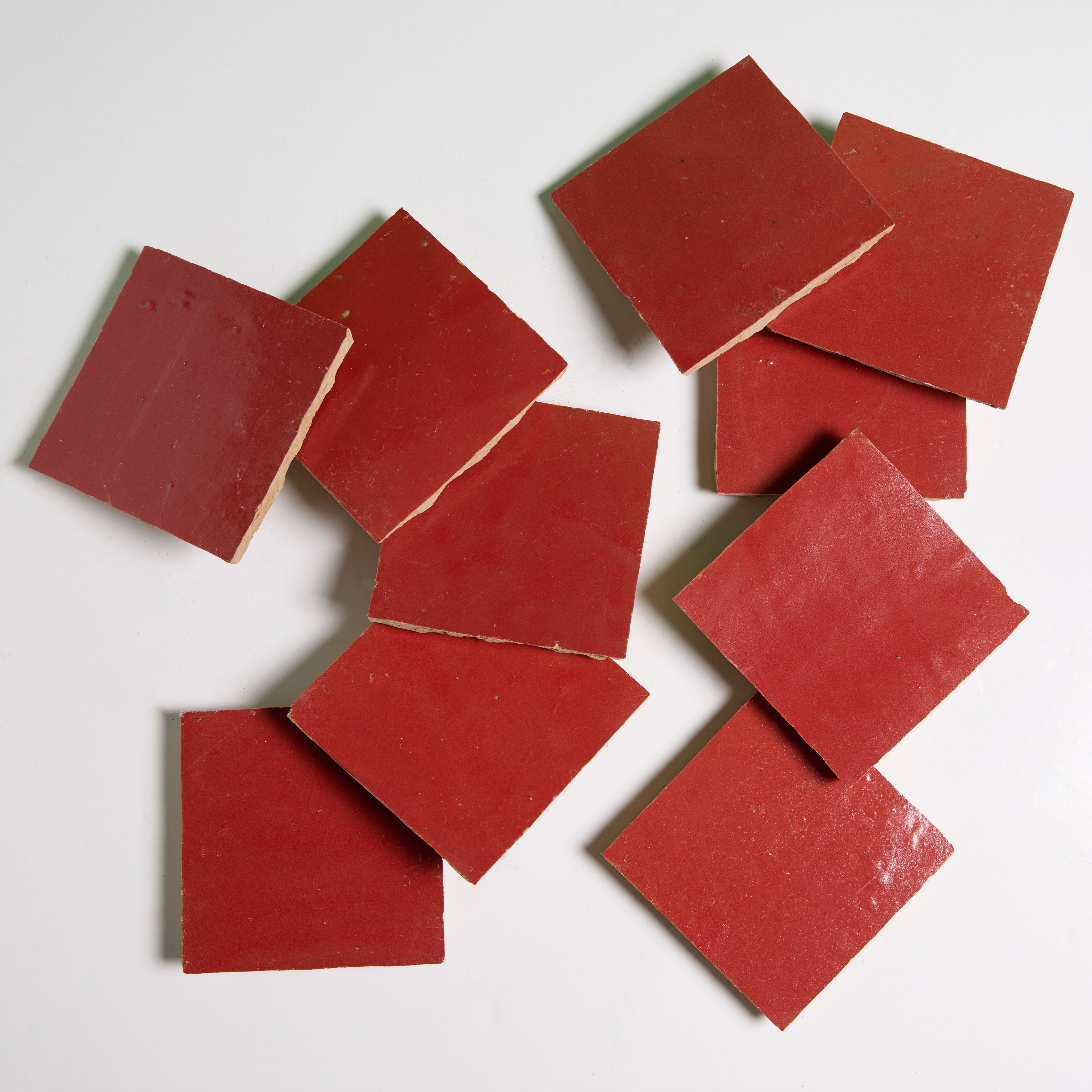 Nine Fiery Red tiles by New York Cement Tile are scattered on a white surface in a slightly overlapping arrangement.