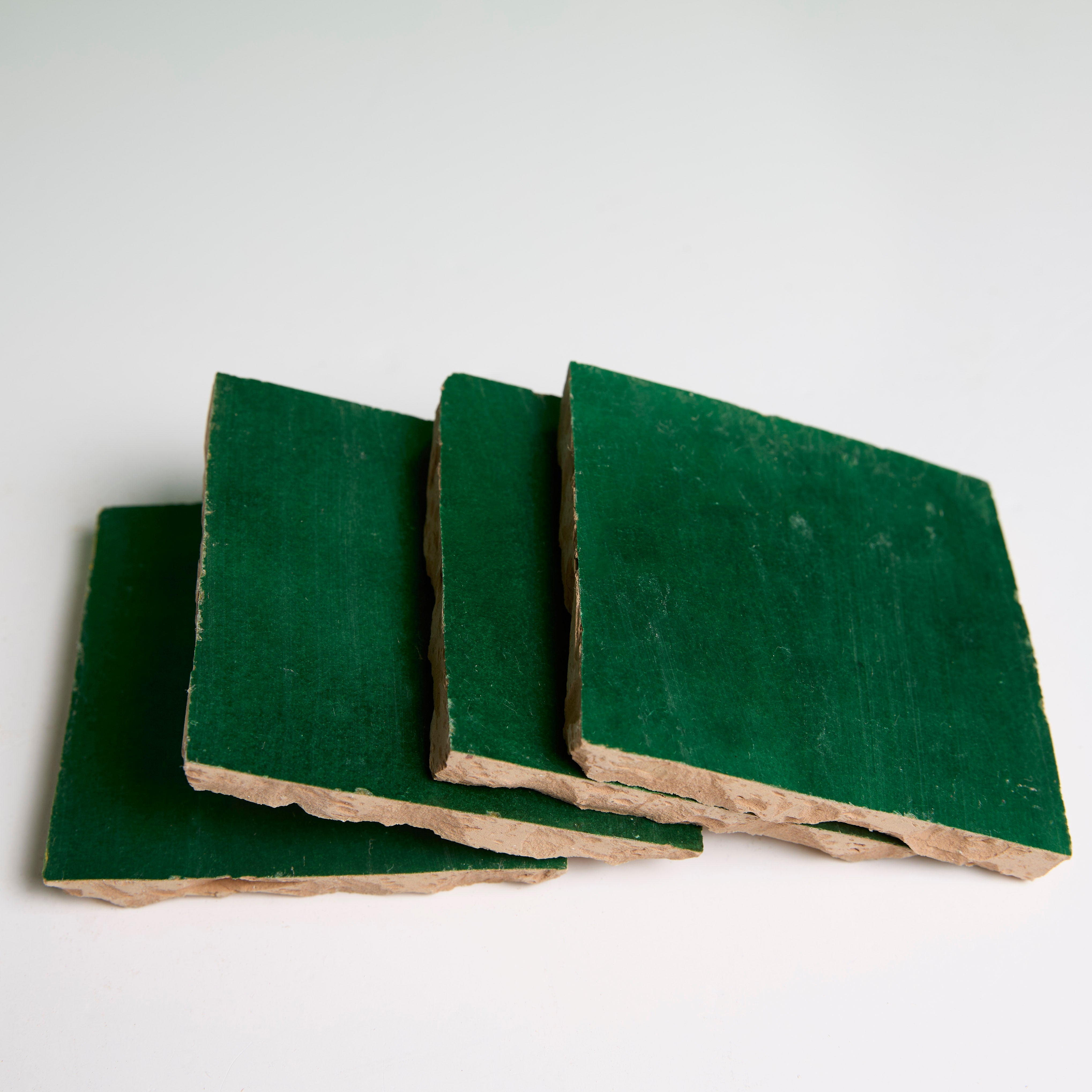 Four Jewel Green Zellige tiles by New York Cement Tile, with rough edges, are stacked on a white surface.