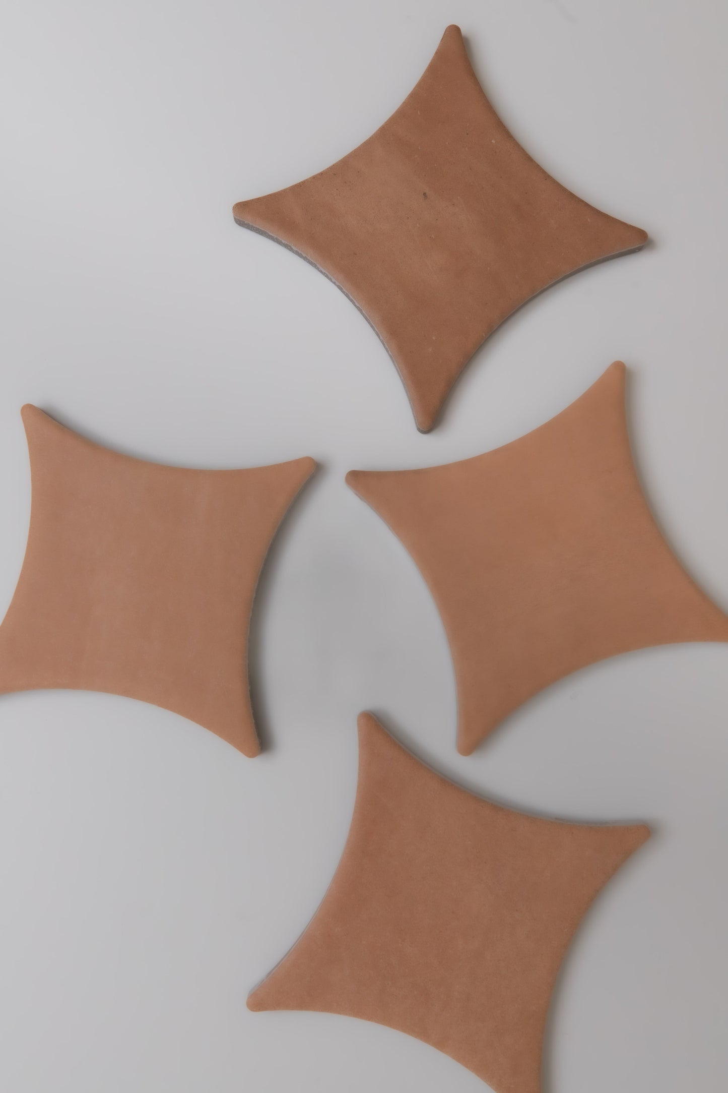 Four tan, diamond-shaped Arcilla ceramic tiles by Finca are arranged on a white background.
