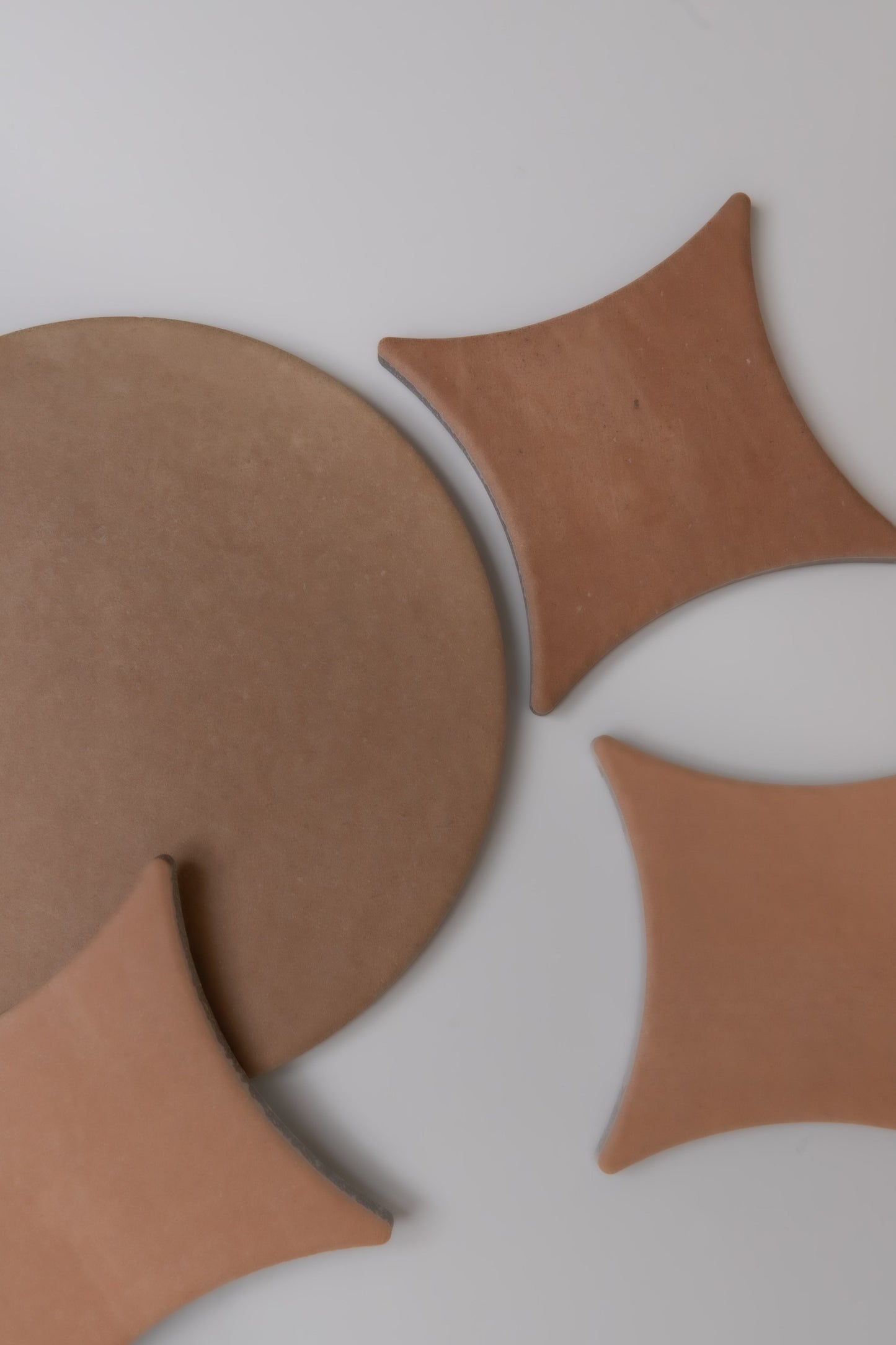 Finca's Arcilla sample tiles, round and curved, are arranged on a light gray surface in an abstract geometric pattern.