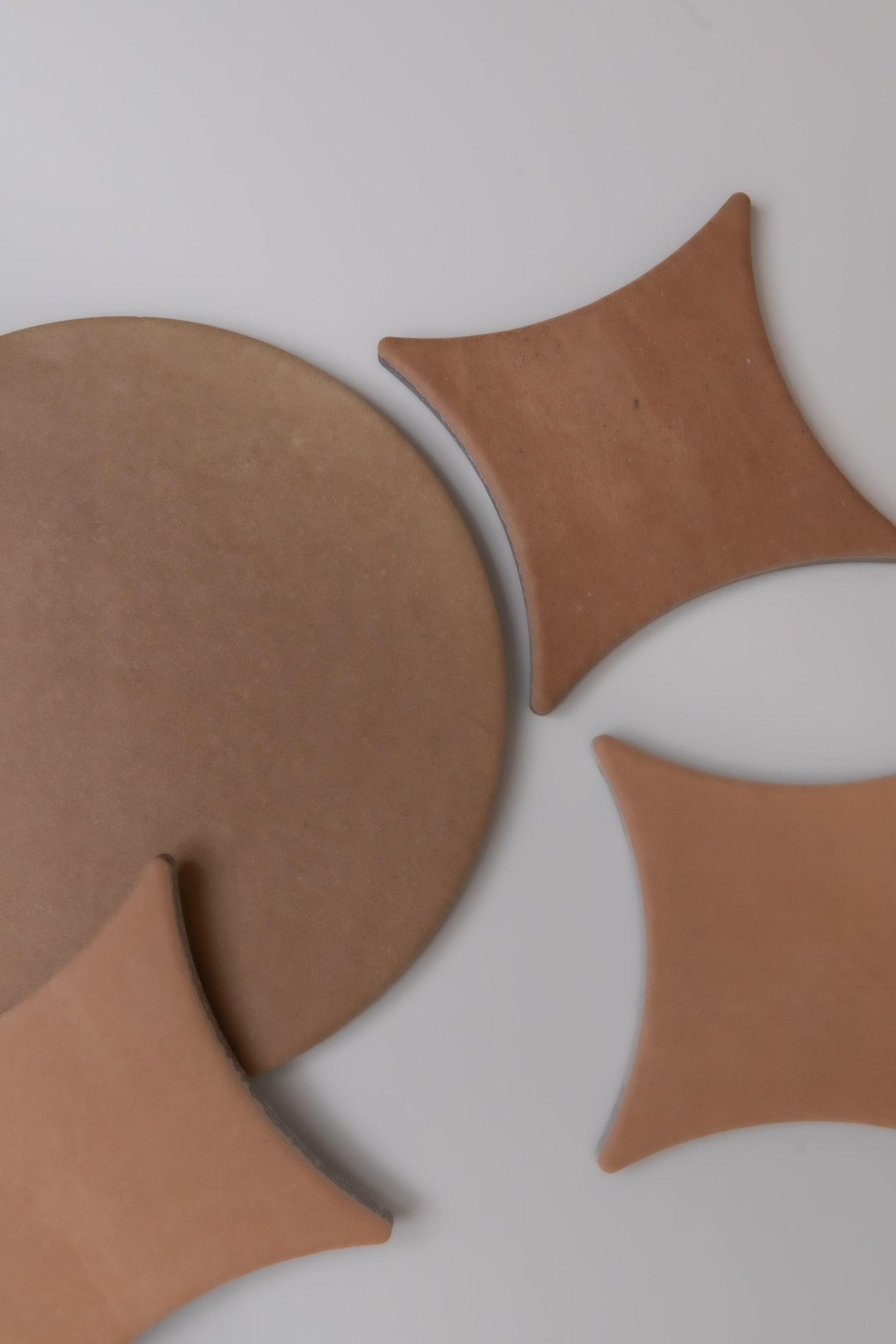 Finca's Arcilla sample tiles, round and curved, are arranged on a light gray surface in an abstract geometric pattern.