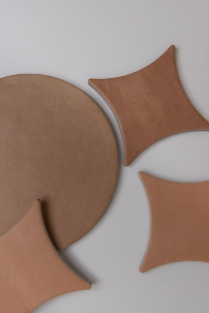 Finca's Arcilla sample tiles, round and curved, are arranged on a light gray surface in an abstract geometric pattern.