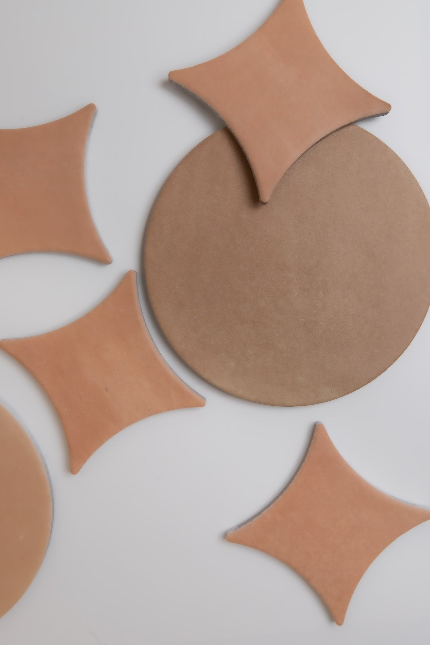 Arcilla sample tiles by Finca, tan round and diamond-shaped, arranged abstractly on a white background.