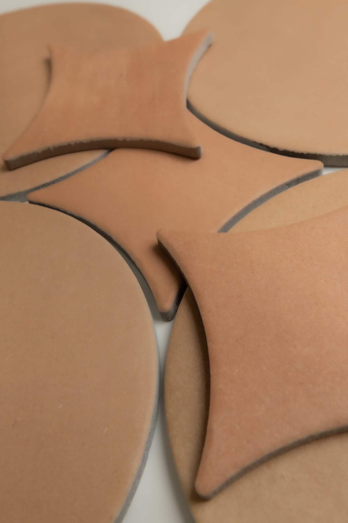 Finca's Arcilla Sample features geometric tan tiles with curved and pointed shapes in an overlapping pattern.