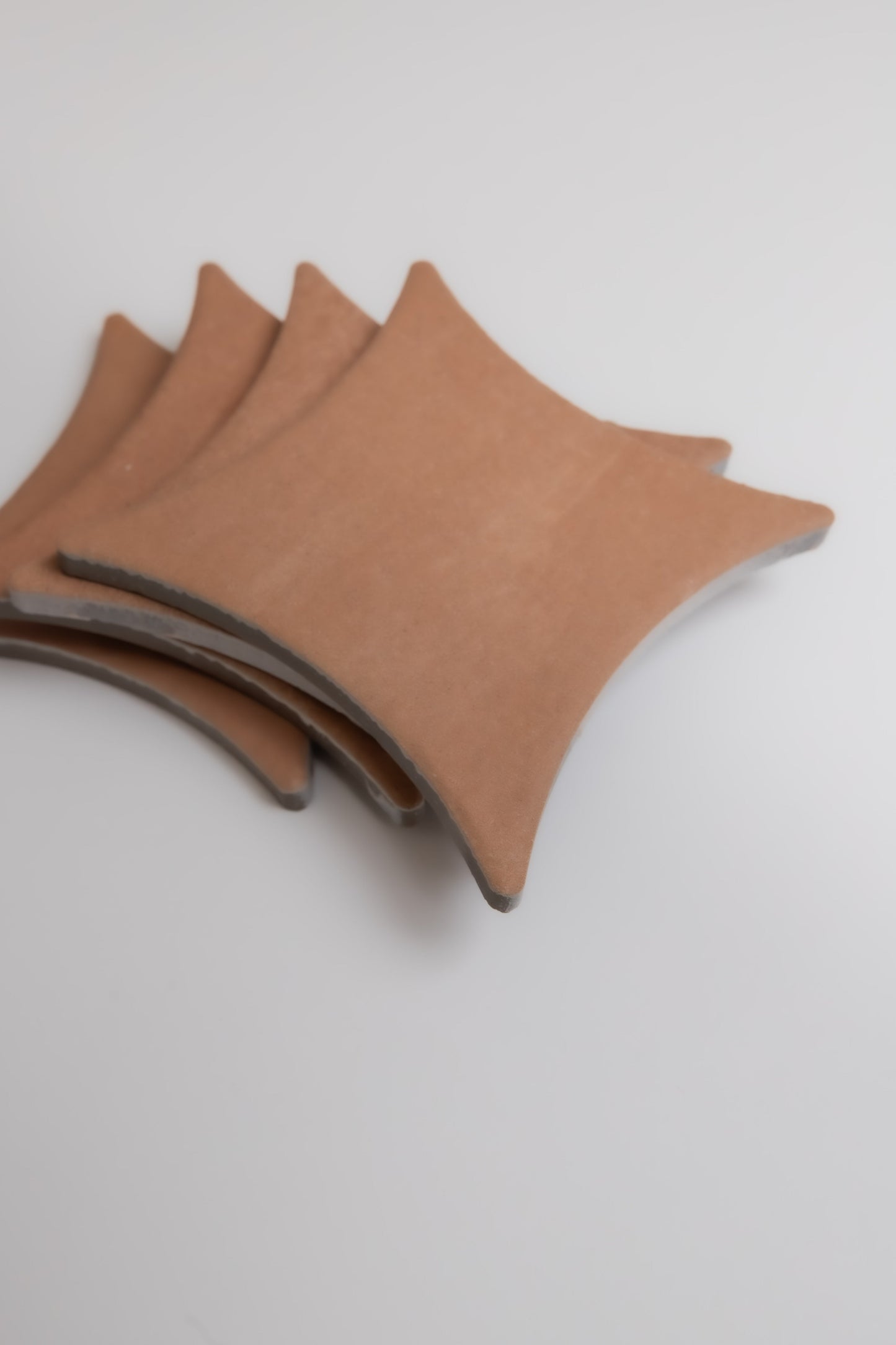 Four brown Arcilla ceramic tiles by Finca are stacked on a white surface with their pointed corners aligned.