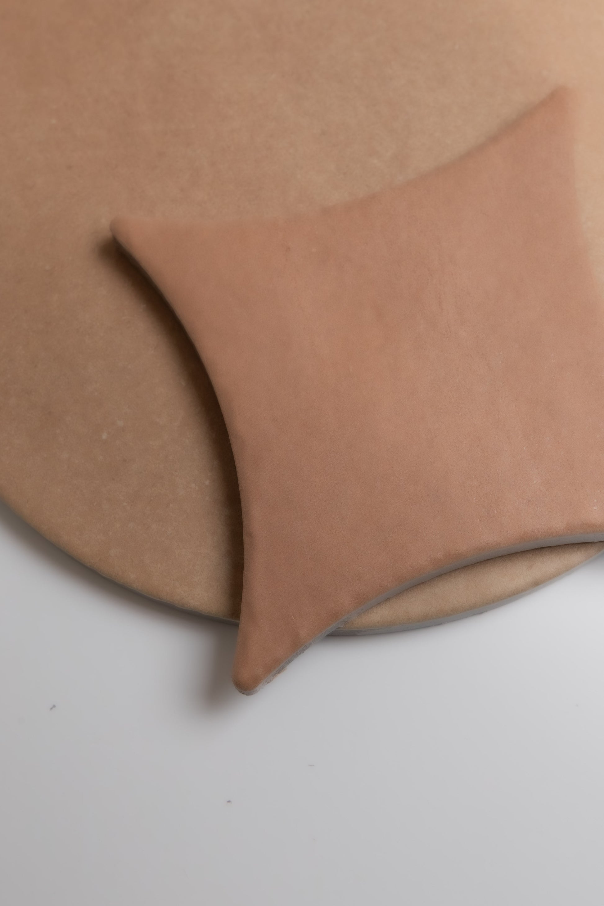 A square Arcilla Sample by Finca sits on a round baking stone, both on a white background.