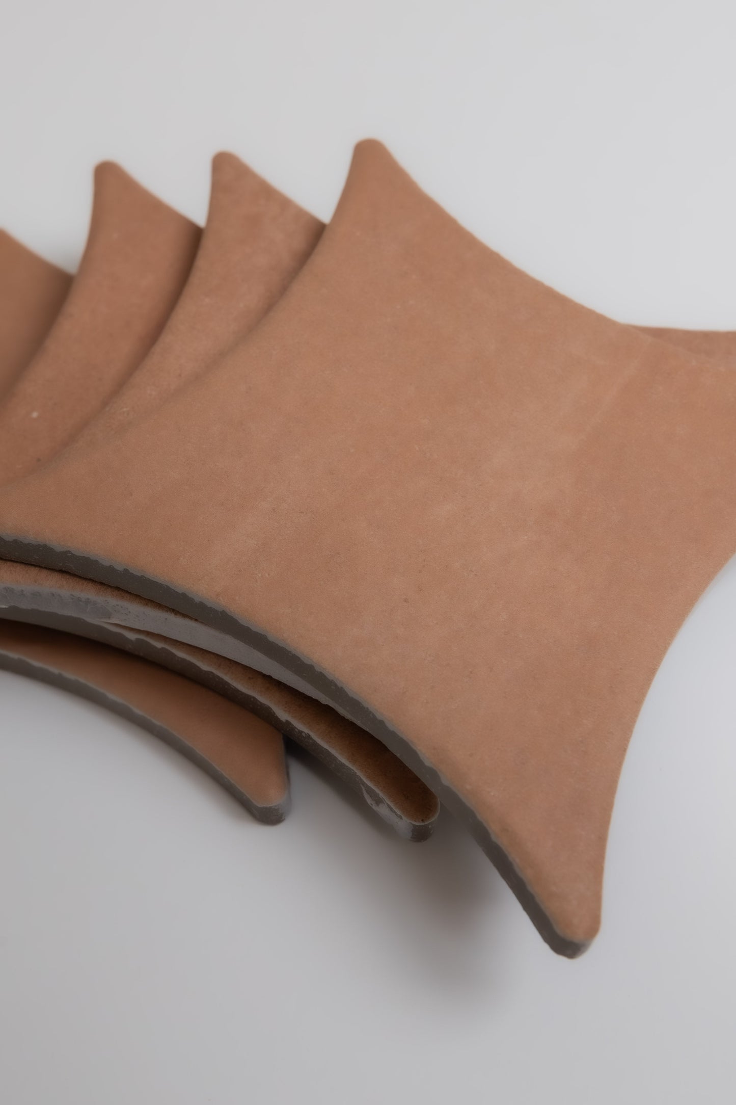 Four Finca Arcilla sample tiles, terracotta-colored and square with curved edges, stacked on a plain light surface.